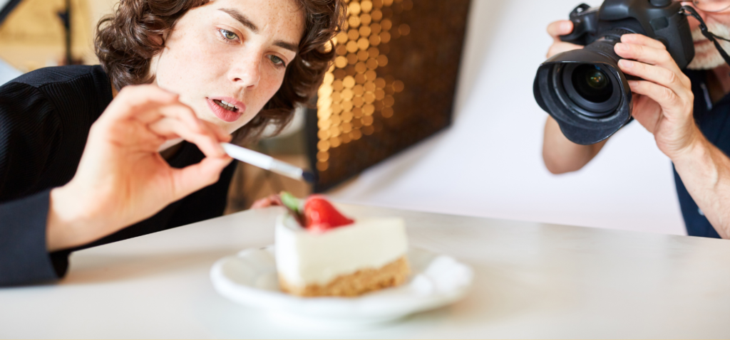 A woman set up the cake, and a photographer took a photo of it using a black camera to market a new restaurant.