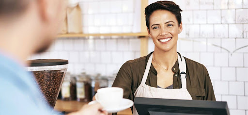Barista with a welcoming smile serving coffee to a customer in a cozy cafe setting.
